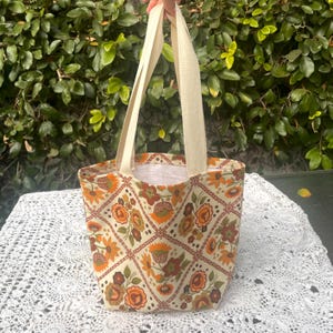 May include: A small, cream-colored tote bag with brown and orange floral print. The bag has two cream-colored straps.