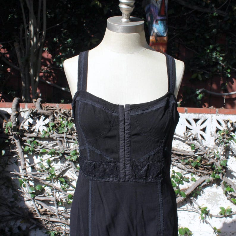 May include: Black dress with spaghetti straps and a fitted bodice. The dress features a decorative lace detail at the waist and a vertical seam down the center of the bodice. The dress is displayed on a mannequin.