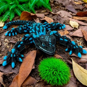 May include: A detailed, articulated black and blue dragon figurine. The dragon has blue accents on its claws, spikes, and head. The figurine is set among fallen leaves and greenery, creating a naturalistic scene.