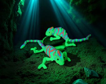 May include: Two neon green and orange striped chameleon figurines rest on a textured green surface. The chameleons are illuminated by a blue light, creating a vibrant and eye-catching display. The scene evokes a sense of mystery and fantasy.