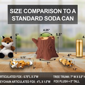 A size comparison chart showing a plush fox, two articulated fox figurines, a tree trunk container, and a standard soda can on a wooden surface. Measurements are labeled: the plush fox is 5" tall, the large articulated fox is 5.75" long by 3" wide, the small articulated fox is 4" long by 1.5" wide, the tree trunk is 7" wide, 5.5" tall, and 4.25" deep, while the soda can is 4.83" tall.