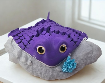 May include: A whimsical purple stingray sculpture with large, expressive eyes and a textured body. The ray rests on a gray rock, with a small blue coral accent. This decorative piece is a charming addition to any coastal-themed decor.
