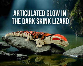 May include: An articulated skink lizard toy with a red, orange, black, and white pattern, resting on a rock in a body of water. The text "ARTICULATED GLOW IN THE DARK SKINK LIZARD" is displayed above the lizard.
