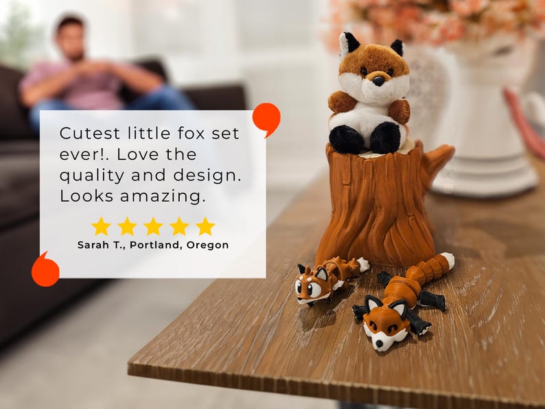 A cozy tabletop scene showcasing a plush fox sitting atop a detailed tree stump container, with two articulated fox figurines posed playfully at its base. To the left, a review quote praises the fox set's quality and design, accompanied by a five-star rating and the reviewer’s name and location. In the blurred background, a person relaxes on a couch, enhancing the warm and inviting feel of the display.