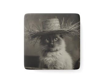 May include: Sepia-toned image of a cat wearing a straw hat with a wide brim. The cat has light-colored fur and dark markings around its eyes and nose. The hat is made of woven straw and has a rustic appearance.