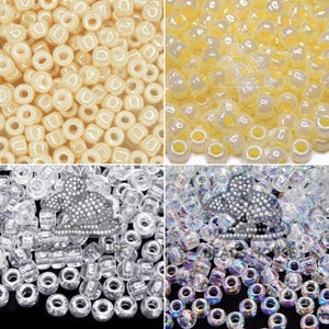 May include: A collection of small, round, hollow beads in four distinct styles: opaque cream, translucent pale yellow, clear glass, and iridescent clear glass, with a small, detailed, white beaded mouse figure resting on the clear beads.