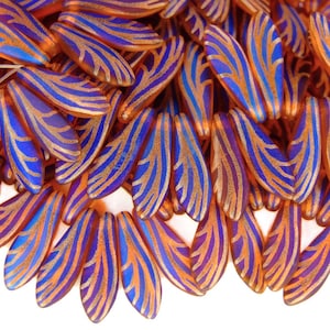 May include: A collection of iridescent, wing-shaped beads. Each bead features a vibrant blue and gold striped pattern over a translucent orange base. The beads are clustered together, showcasing their unique design.