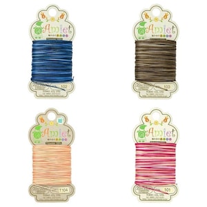May include: Four spools of Amiet polyester thread in shades of blue, brown, peach, and pink. Each spool is labelled with a colour code: 101, 102, 103, and T104. Each spool contains 20 metres/22 yards of thread.