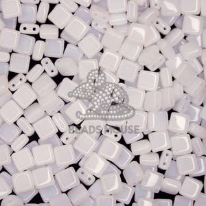 May include: A close-up of a pile of white square glass beads. The beads are opaque and have a slight iridescent sheen.