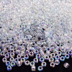 May include: A large quantity of iridescent clear glass beads. The beads are small and round, with a slight shimmer. They are perfect for jewellery making or other craft projects.