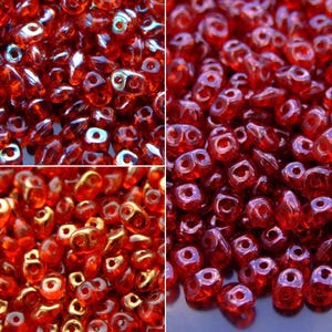 May include: Close-up of a collection of red glass beads. The beads have a double-hole design and a glossy finish. The beads are a deep, rich red color, with some appearing to have an iridescent sheen. The image is a close-up, showing the details of the beads.