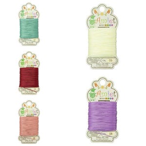 May include: Five spools of Amiet thread in shades of seafoam green, cream, burgundy, peach, and lavender. Each spool is labelled with a colour number and the Amiet logo. The thread is 20m/22yds.
