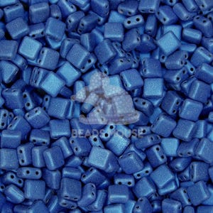 May include: A close-up view of a pile of small, square, blue glass beads. The beads have a matte finish and are slightly iridescent.
