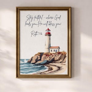 May include: Framed art print featuring a watercolor illustration of a lighthouse on a rocky cliff overlooking the ocean. The lighthouse has a red top and white tower. The print includes the text "Stay faithful - where God leads you. He will bless you! Ruth 1:16."