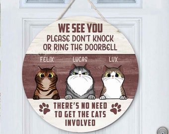 Peut inclure: Une pancarte de porte ronde en bois avec le texte "We see you, please don't knock or ring the doorbell. There's no need to get the cats involved." La pancarte représente trois chats de dessin animé nommés Felix, Lucas et Lux.