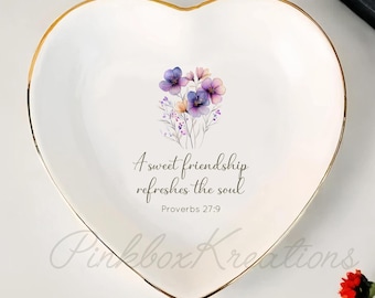 May include: Heart-shaped white ceramic trinket dish with a gold rim. The dish features a floral design in the center and the text "A sweet friendship refreshes the soul" from Proverbs 27:9.