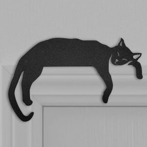 May include: Black metal silhouette of a cat sleeping on a white door. The cat is curled up with its head resting on its paws.