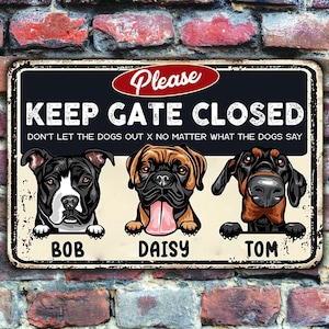 Op de afbeelding: Rechthoekig metalen bord met de tekst "KEEP GATE CLOSED" en de zin "DON'T LET THE DOGS OUT X NO MATTER WHAT THE DOGS SAY". Het bevat illustraties van drie honden genaamd Bob, Daisy en Tom. Het bord staat tegen een bakstenen muur.
