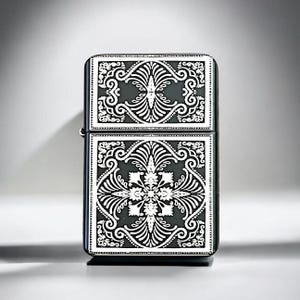 May include: A rectangular metal lighter featuring a black finish with intricate white engraved patterns on the front. The design consists of symmetrical floral and scrollwork motifs divided into two distinct sections by a horizontal line.
