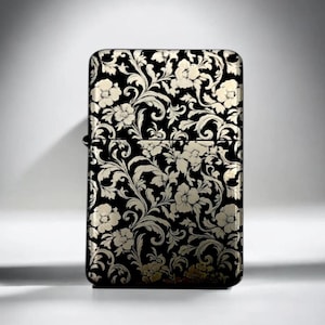 May include: A rectangular metal lighter featuring a black base color with a contrasting metallic silver floral and scrolling vine pattern that covers the entire front surface, including the hinged lid and the main body of the lighter.