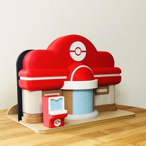 Könnte beinhalten: Eine weiße Keramik-Tasse mit schwarzem Henkel und dem Text "But First, Coffee" in fetter, schwarzer Schrift. Die Tasse steht vor einem verschwommenen Hintergrund, der eine gemütliche Umgebung suggeriert.