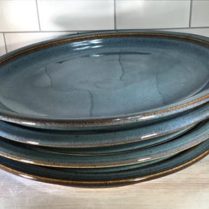 May include: A stack of four blue ceramic dinner plates with brown rims. The plates are glazed and have a rustic look.