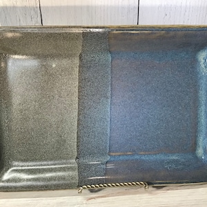 May include: A rectangular ceramic serving tray with two sections, one in a dark gray glaze and the other in a blue glaze. The tray has two rope-like handles on the sides.