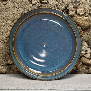 May include: A blue ceramic plate with a brown rim. The plate has a speckled glaze and a slight sheen.