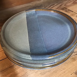 May include: A set of three ceramic plates with a blue and gray glaze. The plates have a gold rim and are stacked on top of each other.
