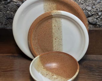 May include: Set of three ceramic plates and a bowl with a speckled brown and white glaze. The plates and bowl have a vertical stripe of a lighter brown glaze.