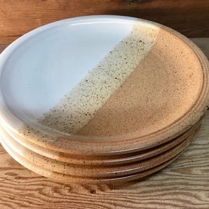 May include: A set of four ceramic dinner plates with a white and brown speckled glaze. The plates are stacked on top of each other.