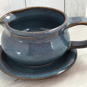 May include: A blue ceramic gravy boat with a brown rim and handle, sitting on a matching saucer.