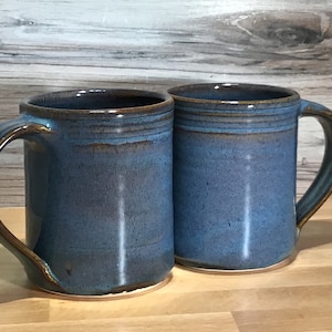 May include: Two blue ceramic mugs with brown accents and a glazed finish. The mugs have a rounded shape and a handle on the side.