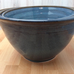 May include: A set of two nested ceramic bowls with a deep blue glaze and a contrasting brown rim. The bowls feature a smooth, rounded shape with a subtle horizontal ridge near the top edge, showcasing a glossy finish and a solid, sturdy base.
