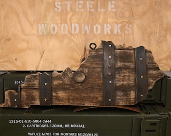 May include: A wooden cutout of the state of Kentucky with metal accents. The cutout is brown and has a distressed finish. The metal accents are black and have a hammered finish. The cutout is mounted on a wooden box with the text "STEELE WOODWORKS" printed on the front. The box is green and has the text "1315-01-618-5864 CA44 2-CARTRIDGES 120MM, HE M933A1 W/FUZE M783 FOR MORTARS M120/M121 LOT GDL19L024-002 WT 97.40 LBS" printed on the front.
