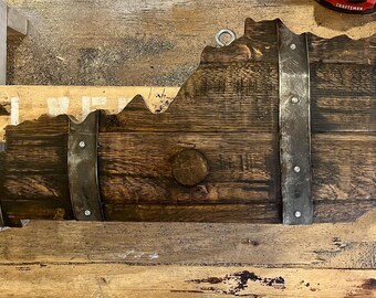 May include: A wooden state of Kentucky shaped like a barrel with metal bands and a dark brown stain. The state is hanging on a wall.