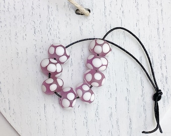 May include: A strand of pink and white polka dot glass beads on a black cord. The beads are round and have a glossy finish.