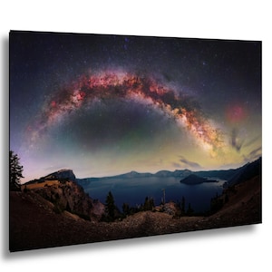 May include: A panoramic wall art print featuring a dark blue lake surrounded by rugged cliffs and silhouetted trees under a night sky. A vibrant, arched band of the Milky Way galaxy stretches across the horizon, displaying hues of pink, orange, and white.