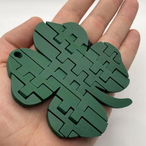 May include: A green four-leaf clover shaped puzzle made of interlocking pieces. The puzzle is made of plastic and has a smooth, matte finish.