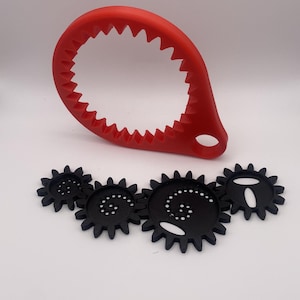 May include: A red, serrated jar opener and four black gear-shaped coasters. The jar opener is a curved, loop-shaped tool with a hole for hanging. The coasters have a spiral design with small white dots.