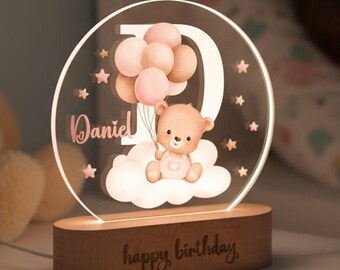 May include: A personalized night light with a wooden base. The clear acrylic light features a teddy bear holding balloons, the name "Daniel", the number "9", and the words "happy birthday". The light is on a white nightstand.