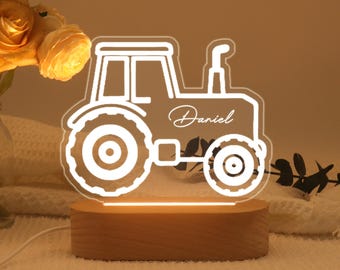 May include: A tractor-shaped night light with the name "Daniel" in script. The light is white and sits on a rectangular wooden base. The tractor design includes large wheels and a detailed outline.
