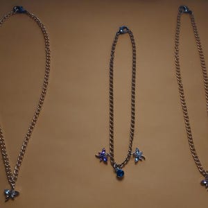 以下が含まれることがあります： 蝶とトンボのチャームが付いたゴールドチェーンネックレス3本。チャームは青、紫、ピンクの宝石で飾られています。