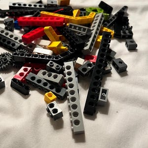 May include: A collection of gray, black, red, yellow, and white Lego pieces. The pieces include various sizes and shapes of bricks, beams, and connectors.