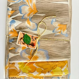 May include: A bundle of vintage fabric featuring floral patterns in shades of beige, orange, and blue. The fabric is tied with yellow twine and includes a tag with a cartoon turtle and the words "Full Turned Turtle".