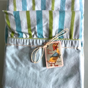 May include: A folded blue and green striped twin-sized bed sheet with a tag that says "Silly Goose Twin".