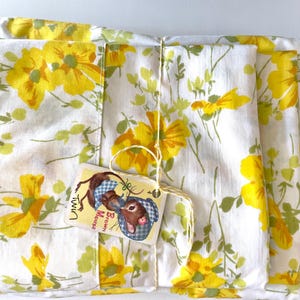 May include: A set of twin-sized bed sheets with a white background and a yellow floral pattern. The sheets are folded and tied together with a string. A small tag with a cartoon mouse is attached to the string. The tag reads "Brown Mouse".