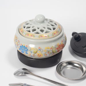 Può includere: Un bruciatore di incenso in ceramica bianca con un design floreale e una base nera. Viene fornito con un porta incenso in metallo, un cucchiaio e delle pinzette.