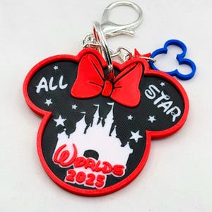 May include: Red and black Mickey Mouse-shaped keychain with a white castle silhouette, a red bow, and the text "All Star Worlds 2023".