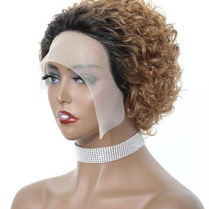 Puede incluir: Peluca corta y rizada con una mezcla de tonos marrones y rubios. La peluca presenta un frente de encaje para una apariencia natural. La modelo lleva un collar de gargantilla de diamantes de imitación plateados. La peluca está peinada en un corte pixie corto.